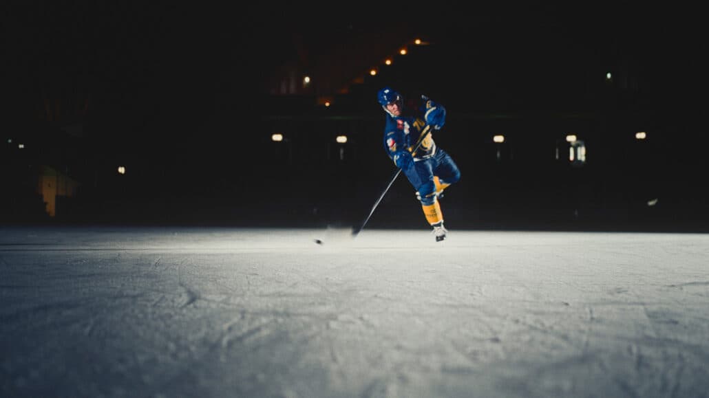 Hockeyspieler des HC Davos sprintet über dunkles Eis, Eisstaub im Gegenlicht